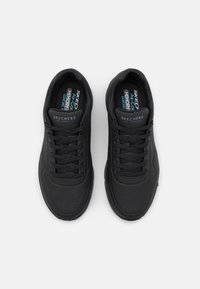 Black athletic shoes with a textured synthetic upper, featuring a lace-up design and perforations for breathability. Memory foam insoles visible.