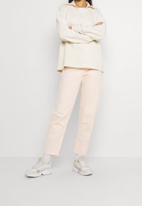 Ljust beige tröja med halvmidja och krage, vita detaljer, i kombination med mjuka rosa byxor och vita sneakers med grå detaljer.