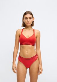 Sarkans kokvilnas bralets ar regulējamiem siksnām un Calvin Klein logotipa joslu. Saderīgi sarkani apakšbikses ar logotipa jostu, abas izgatavotas no gludas, elastīgas tekstūras.
