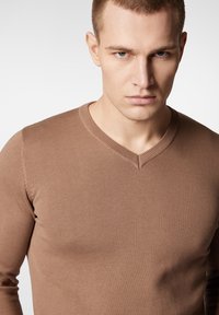 Brązowy, dopasowany sweter z dekoltem w serek. Posiada strukturalny ryżowy wzór i detale szycia wzdłuż rękawów. Prosty i minimalistyczny styl.