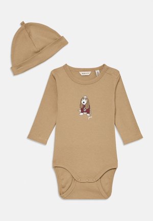 Body de bebé de manga larga en color beige con botones de presión y gorro a juego, con un dibujo de un perro animado que lleva un suéter burdeos en el frontal.