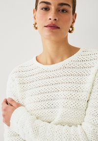 Maglione bianco lavorato a maglia con texture a trama aperta, scollatura rotonda e polsini a coste. Il modello presenta una vestibilità rilassata e un design minimalista.