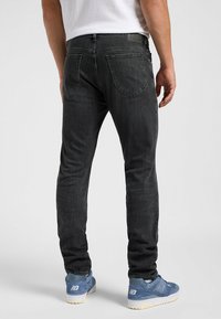 Slim-fit zwarte jeans van denim, met achterzakken met subtiele stiksels, gedragen met blauwe sneakers.