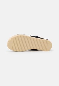 Espadrille negra con suela texturizada y detalles de yute. La suela es de un beige claro y cuenta con estrías horizontales para mayor agarre.
