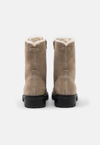 Kotníkové boty z taupe semiše s ovčí kožešinovou podšívkou, černými gumovými podrážkami a dvojitými bočními zipy pro snadný přístup.