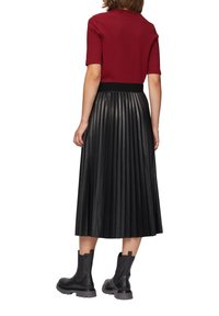 Rood geribbeld t-shirt met korte mouwen gecombineerd met een zwarte geplooide leren rok en zwarte enkelboots. Accentdetails zijn onder andere een aansluitende tailleband.