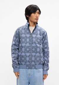 Μπλε φερμουάρ τζάκετ με σχέδιο με μοτίβα και λογότυπα, ριμπ μανσέτες και στρίφωμα, και στάνταρ γιακά. Λείες υφή με casual γραμμή.
