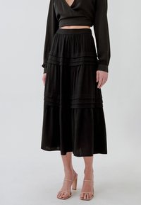 Gonna nera a balze realizzata in tessuto leggero, con pieghe orizzontali e vita elastica. Abbinata a un top nero corto e sandali con cinturini.