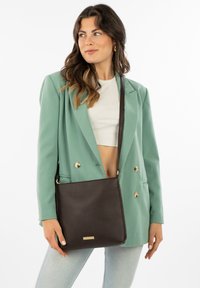 Brown leather shoulder bag with textured finish, gold accent, and stitched edges, paired with a mint green blazer and a white top.