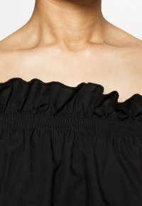 Schwarzes, schulterfreies Oberteil mit Rüschenausschnitt, elastischem Smocking und leichtem, strukturiertem Stoff. Nahaufnahme der Stoffdetails.