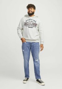 Hanorac gri cu branding imprimat, asortat cu blugi deinostiți albastre și adidași negri cu talpă albă. Stil casual, croiala lejeră.