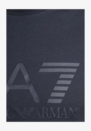 Dunkler Stoff mit großem, stilisiertem "A7" und schwachem "Armani"-Logo mit einem Adleremblem unter den Buchstaben.