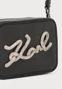 Borsa a tracolla in pelle nera texturizzata con un adornamento in strass argentati "Noel" sul davanti. Presenta una tracolla rimovibile e una chiusura con zip.