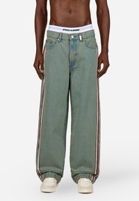 Svijetloplave široke traperice izrađene od denima, s dvije vertikalne pruge u crvenoj i bijeloj boji s obje strane, s bijelim PEGA-DOR pojasom.