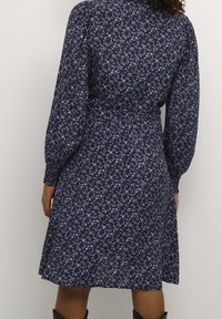 Abito nero floreale con maniche a sbuffo lunghe e vita aderente, caratterizzato da motivi viola e verdi. Tessuto morbido e leggero.