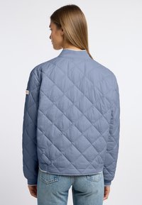 Jasnoniebieska pikowana kurtka z diamentowym wzorem, prążkowanym kołnierzem i mankietami, z naszywką z logo na lewym rękawie.