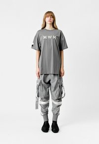 Camiseta gris de gran tamaño con el logo "MWM", combinada con pantalones cargo grises que cuentan con múltiples bolsillos y correas. Calzado texturizado negro.