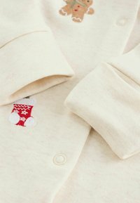 Cremfarbener Baby-Body mit Druckknöpfen, verziert mit gestickten roten Weihnachtsstrümpfen und Lebkuchenmann-Dekorationen.