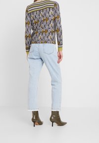 Langarm-Pullover mit einem Blattmuster in Grau und Senf, kombiniert mit hellblauen Jeans und olivgrünen Stiefeletten mit Stöckelabsatz.