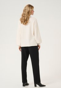 Maglione cremoso, strutturato, di grande dimensione con maniche a palloncino, abbinato a pantaloni neri su misura e stivaletti neri con tacco.