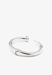 Brazalete de plata con un acabado liso y pulido, que presenta un diseño abierto distintivo y un detalle en el extremo puntiagudo, fabricado en metal.