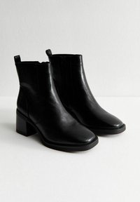 Zwarte leren enkelboots met een blokhak, een gladde afwerking, zijritsen en kleine lusjes aan de achterkant.