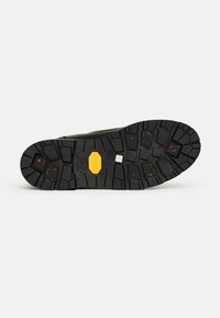Crna guma đona s dubokim utorima, koja sadrži žuti Vibram logo. Hemisferične i kružne površine poboljšavaju prianjanje. Teksturalni detalji dizajna.