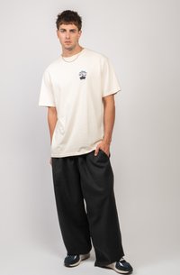 T-shirt in cotone color crema con un piccolo design di bonsai ricamato in blu sul petto, abbinato a pantaloni neri oversize.