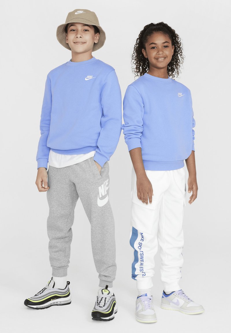 To barn står side om side iført lyseblå Nike hettegensere, grå og hvite Nike bukser, og sportssko, og smiler til kameraet.