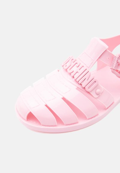 Sandale en caoutchouc rose brillant avec plusieurs brides et une boucle, arborant le logo "MOSCHINO" en relief sur la bride supérieure.