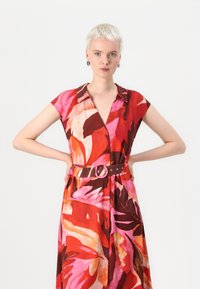 Robe florale en dégradés de rouge, rose et marron avec une ceinture dotée d'une boucle ronde. Manches courtes et col, avec un design fluide.