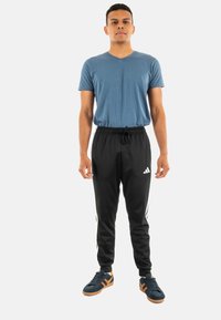 Blauwe V-hals t-shirt, zwarte sportbroek met witte strepen, en blauwe sneakers met oranje accenten. Verstelbare trekkoord taille.