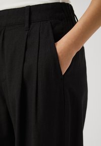 Svarta linnebyxor med avslappnad passform, med framveck och sidofickor. Tyget har en texturerad, något rynkig look.