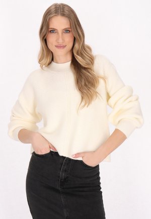 Crème geribbelde trui met een hoge hals en verlaagde schouders, in combinatie met een zwarte denim rok. Zachte textuur en een relaxte fit.