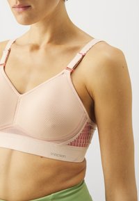 Lyserosa mesh-bh med sømløs design, justerbare stropper og en teksturert band med logo. Minimalistisk stil med støttende konstruksjon.