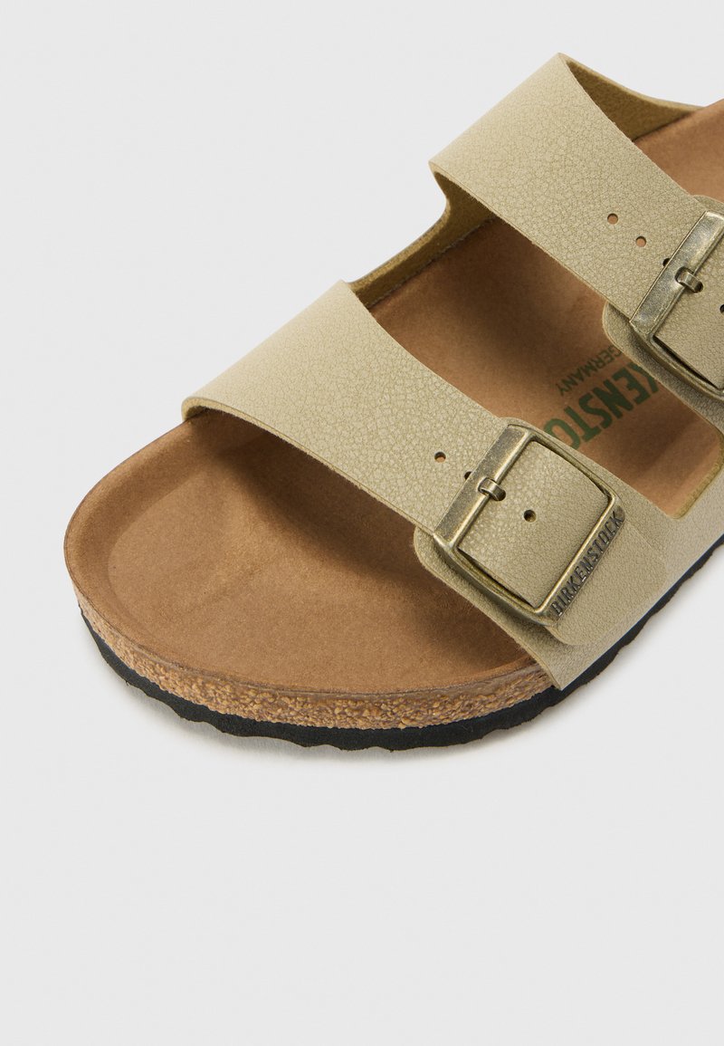 Sandal beige a due cinturini con tomaia sintetica testurizzata, fibbie in metallo e un plantare in sughero marrone su una suola in gomma nera.