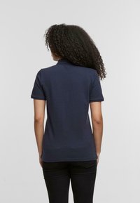 Granatowa koszulka polo z krótkimi rękawami, kołnierzykiem i prostym dołem; noszona z czarnymi spodniami; gładki materiał i minimalistyczny design.