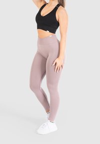 Schwarzer gerippter Sport-BH kombiniert mit hochgeschnittenen, hellrosa Leggings. Glatte Textur, einfarbige Farben und weiße Sneaker mit Logo-Akzenten.