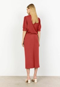 Completo rosso a due pezzi composto da una maglietta a maniche corte con maniche a sbuffo e una gonna fino al ginocchio, realizzato in morbido tessuto. Sandali con tacco a blocco spesso.