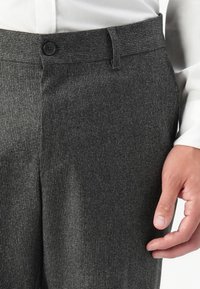 Pantalons gris texturés avec un devant plat, fermeture à bouton et taille standard. Le matériau est un tissage subtil, offrant une apparence structurée.