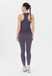 Lila Sport-Top mit Racerback-Design, kombiniert mit passenden lila Leggings und silbernen Laufschuhen. Glatte, enganliegende Materialien.
