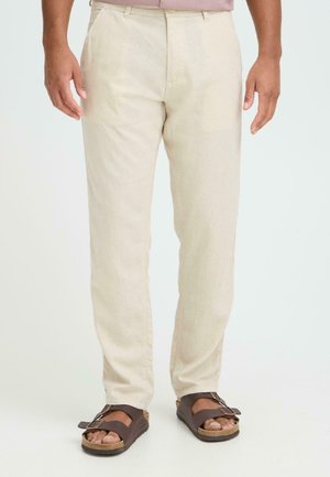 Lyse beige linnedbukser med lige ben, der har forlommer og en glat tekstur. Parret med mørkebrune sandaler med spænde.