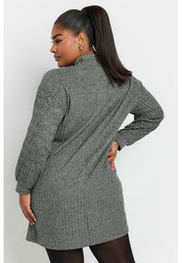 Abito maglione grigio a coste con maniche lunghe, scollo alto e tasche laterali. Tessuto morbido con un fit ampio.