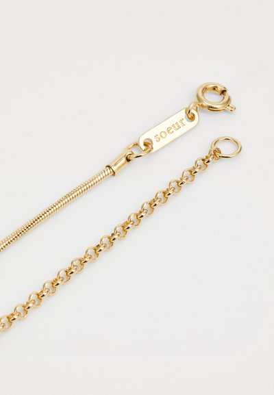 Guldbelagt armbånd med en kæde og slangedesign. Låsen har et graveret mærke med teksten "søster." Glat overflade og skinnende finish.