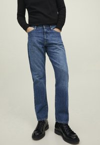 Blå denimjeans med avslappet passform, fremtredende sømmer og design med fem lommer. Kombinert med svarte snøresko.