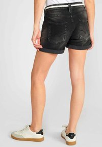 Shorts en denim noir avec un ourlet retroussé, dotés de deux poches arrière avec un motif brodé subtil, associés à des baskets blanches.