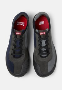 Svarta, grå och marinblå mockasneakers med svarta snören och röda innersulor. Etiketterna säger "CAMPER" och "TWINS." Designade för avslappnad användning.