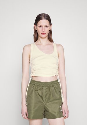 Top court jaune clair en tissu côtelé avec liens sur les côtés, associé à un short vert olive à taille élastique offrant une finition lisse.