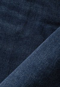 Tejido de mezclilla azul oscuro con superficie texturizada, que muestra un leve brillo y un patrón tejido, doblado para revelar profundidad y suavidad.