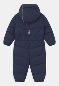 Granatowy puchowy kombinezon narciarski z kapturem; posiada elastyczne mankiety i pas. Mały wzór rakiety nadrukowany na plecach. Miękki, izolowany materiał.